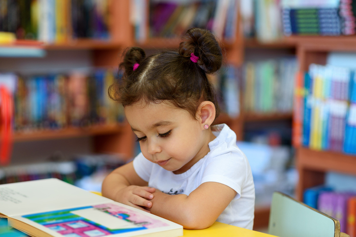 A little girl sitting at the table in front of a book.